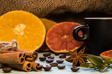 A black mug of coffee next to cinnamon with puddings and chopped oranges