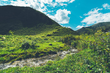 Fototapeta na wymiar Beautiful scenery with brook surrounded by hills, native grasses, and pastures; wide-angle view of landscape with mountain stream and hills ridge in the background, surrounded by feeding ground