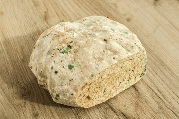 Moldy and musty round wheat bread on wooden background