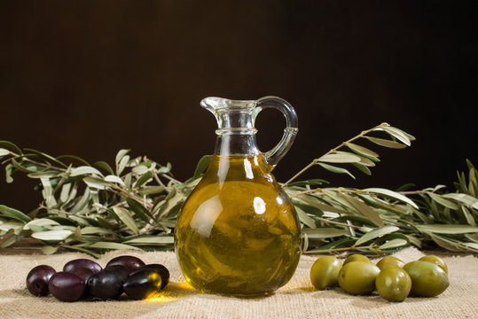 Virgin olive oil glass jar and leaves with fresh olives.