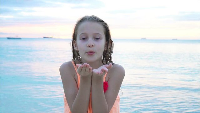 Adorable little girl at beach having a lot of fun at sunset. Happy kid looking at camera and kissing background beautiful sky and sea. SLOW MOTION
