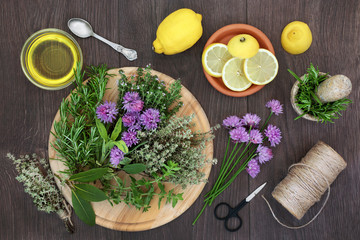 Herb seasoning with fresh herbs also in flower with lemon fruit and olive oil, with string and scissors to hang and dry leaves. On rustic oak wood background, top view.