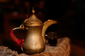 Tea pot / Old tea pot is standing on the edge of fireplace with a tea cup full of tea in the background, Aqaba, Jordan