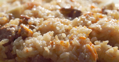 Pilaf from rice and meat with the addition of carrots and garlic. Prepared meal before consumption, fatty product close-up.