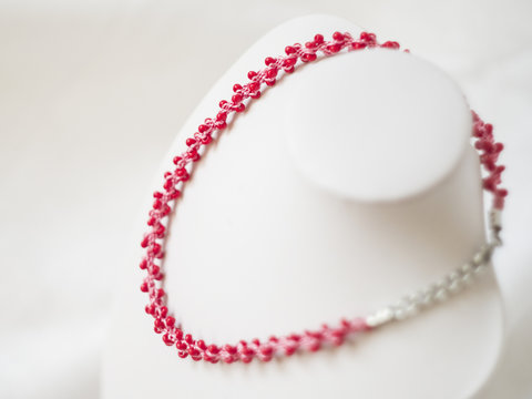 pink necklace with red beads on white stand