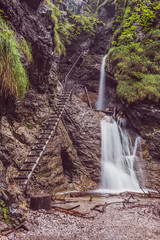 Fototapeta premium Wodospad w Parku narodowym - Słowacki Raj. Drabina na szlaku w skalnym wąwozie, prowadząca w górę wodospadu.