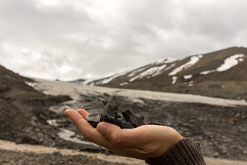 Female hand holding coal found by the Longyear glacier, wich is seen in the background. Arctic landscape of glacial moraine stones and mountains, Longyear valley, Svalbard.