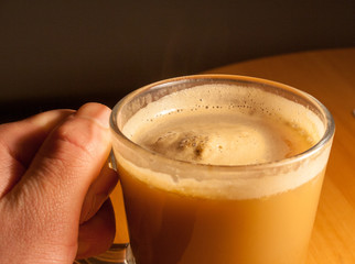A glass of cappuccino in the palm of your hand. Texture of orange foam.