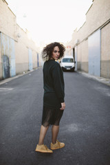 Close-up portrait of young girl wearing green dress and yellow shoes. Pretty female with curly hair looking at the camera. Woman in urban background.