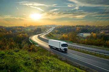 Foto op Aluminium Witte vrachtwagen rijden op de snelweg kronkelend door bebost landschap in herfstkleuren bij zonsondergang © am