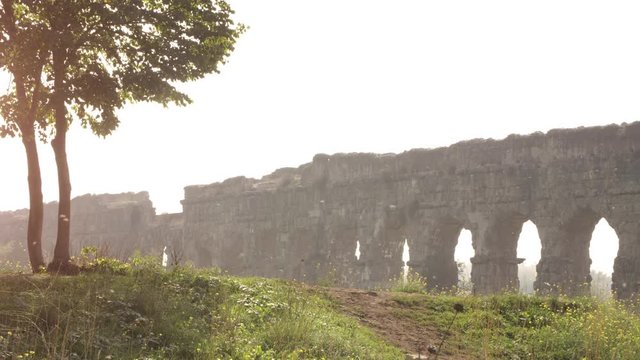 Stunning view of roman aqueduct claudio ruins arches in parco degli acquedotti park ruins in rome on romantic misty sunrise landscape with hill dirt road and trees