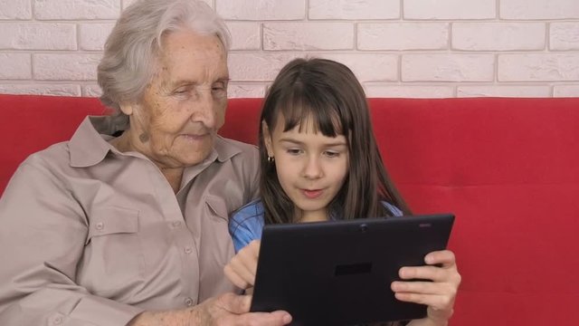 An elderly and a child with a tablet .The little girl is teaching an elderly woman on a tablet.