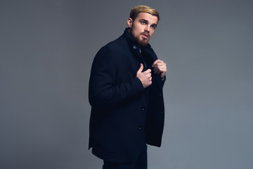 Young and handsome. Attractive business man holding lapels standing in front of grey background