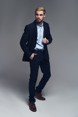 Stylish and professional. Fashionable entrepreneur holding lapel and put the other hand into the pocket in front of grey background.