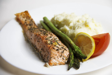 Cooked, fried, grilled salmon fish fillet with potatoes, asparagus, tomato and lemon slice on a plate. White background.