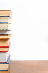 Stack of different books on a table against a white wall background
