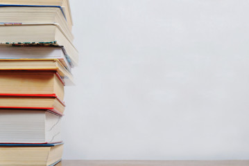 Stack of different books on a table against a white wall background