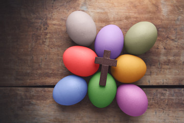 Wooden cross above the colored Easter eggs on wooden background
