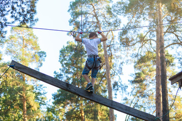 cute boy  climbs on a very risky treetops in rope adventure park in the summer