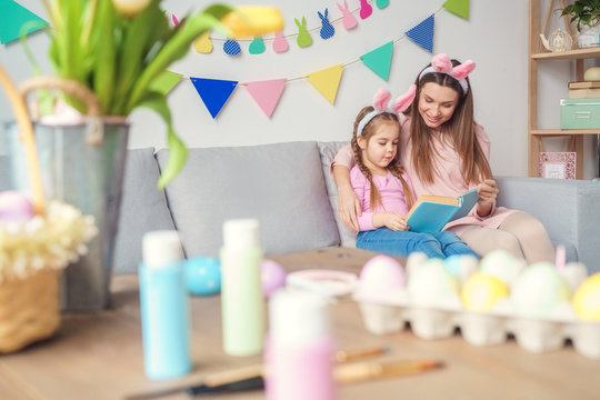 Mother And Daughter Together At Home Easter Preparation In Bunny Ears Reading Book