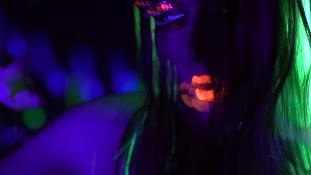 Fashion model girl with colorful fluorescent makeup in ultraviolet neon lights. Female disco dancer in UV light. Night club, party. 4K UHD video footage. 3840X2160