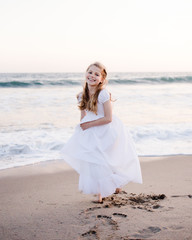 Young girl wearing white dress twirling on the beach with ocean in the background