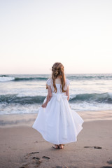 Fototapeta na wymiar Young girl in white dress looking out into the ocean from the beach