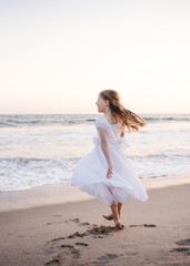 Young girl twirling on the sand next to the ocean