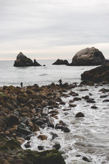 A far away child and an adult walking over rocks leading to the ocean