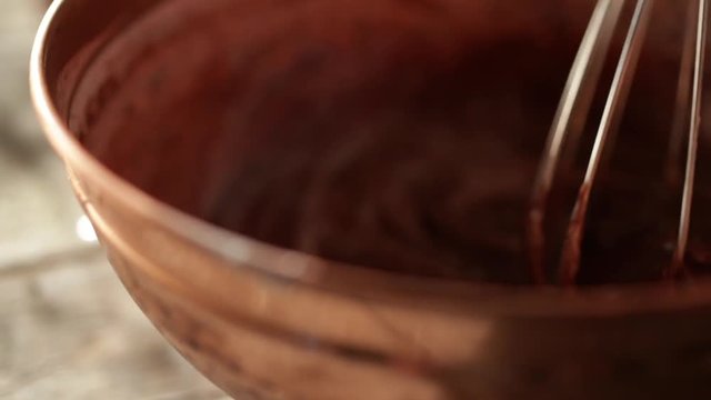 Wire whisk mixes chocolate in mixing bow, slow motion