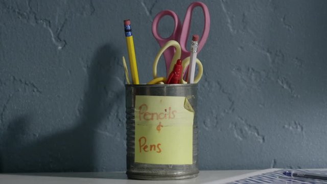 Girl's hand reaches and takes a pencil out of a can