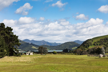 Fototapeta na wymiar Farm house and paddock in rural Otago Peninsula, New Zealand, with coastline and mountains in distance