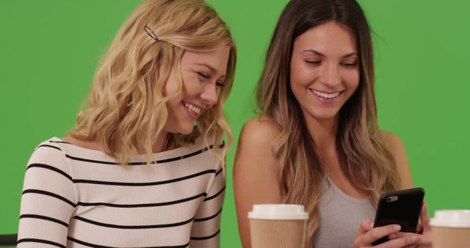 Close-up of two attractive women looking at smartphone pictures on greenscreen