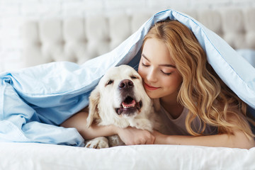 Beautiful teen girl with golden retriever dog in a bed