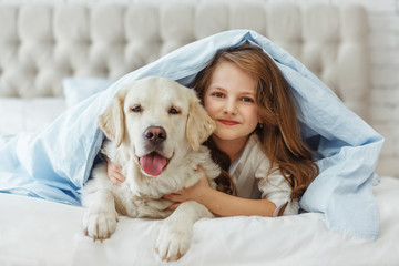 Obraz premium Beautiful little girl with golden retriever dog in a bed