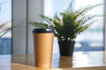 A glass of paper with a drink, coffee, tea, mors from the coffee shop, bar, catering, take-away. Waiting, loneliness, sunny day, morning, day meals. Horizontal. In the background, a plant With lid © Ekaterina