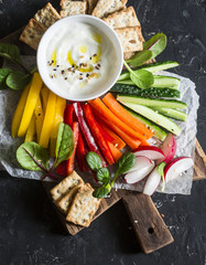 Weight loss concept of a healthy diet food. Mix vegetables and greek yogurt sauce on a wooden rustic cutting board. Sweet pepper, carrot, cucumber, radish and yogurt sauce. Flat lay