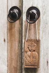 Wooden plate in balinese stile hanging on metal door knob. Textured background. Old rustic style. Don't disturb sign symbol