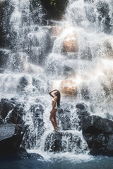 Naklejka na ściany i meble Woman enjoying under stream of big and beautiful cascade waterfall. Girl with slim body and long hair. Kanto Lampo in Ubud area