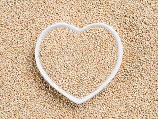 Quinoa in heart-shaped bowl on quinoa background