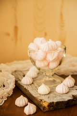 Gentle dessert. Meringues with taste of cranberries in a glass vase on a white tray on a light wooden table.