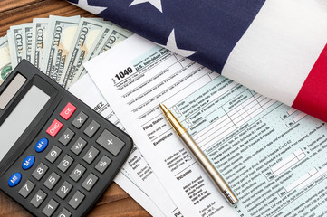 Tax forms with pen, calculator, money and american flag on the table.