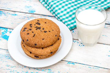 Plate with chocolate chip cookies, glass of milk and kitchen towel on the old blue wooden table.