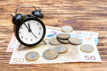 Alarm clock with euro bills and coins on the wooden table. Business concept.