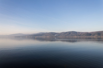 Naklejka na ściany i meble Beautiful view of Trasimeno lake (Umbria, Italy), with hills and blue sky reflecting on water