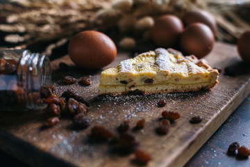 Traditional italian cake with ricotta cheese and raisin, eggs, jar and powdered sugar on wooden background, selective focus