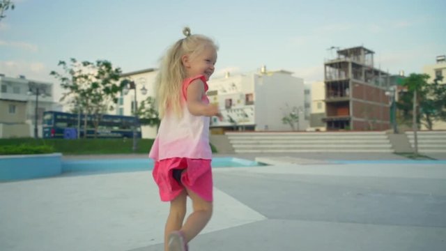 Funny baby girl runs away from camera at playground at sunset rapid slow motion