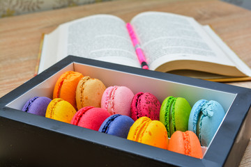 Colorful macaroons for breakfast - on a background of a book with a pencil.