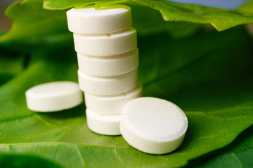 Fototapeta na wymiar a pillar made of medical tablets which is covered with a green leaf, a pill lying on a green leaf