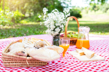 Healthy food and accessories outdoor summer or spring picnic, Picnic wicker basket with fresh fruit, bread and a glass of refreshing orange juice in the camping nature background